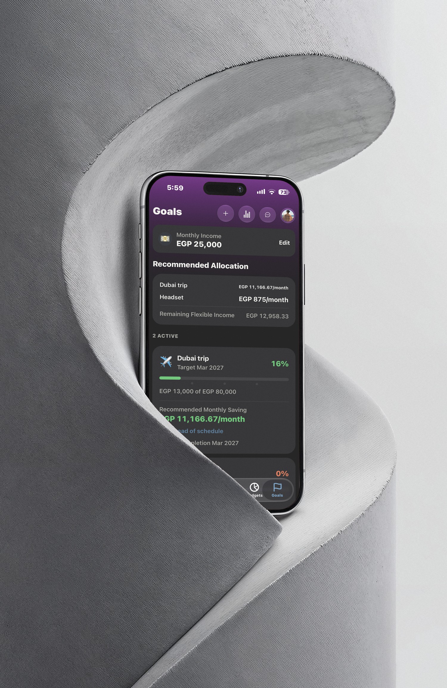 AIVA goals screen showing recommended monthly allocation and goal progress, on an iPhone set into a folded paper sculpture