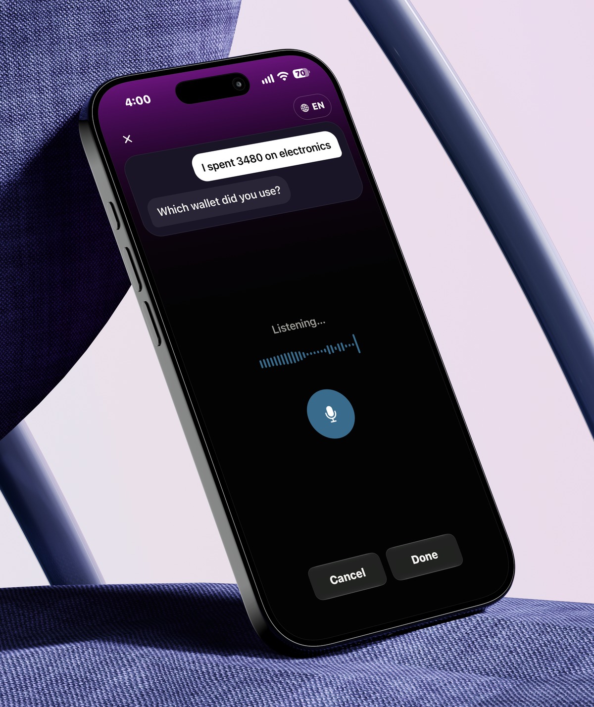 AIVA voice input screen showing a spoken transaction and a follow-up question about which wallet was used, on an iPhone leaning against a chair
